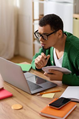 Genç bir adam rahat bir evde dizüstü bilgisayarına notlar alıyor..