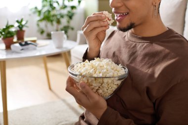 Rahat bir ortamda genç bir adam evde rahat rahat otururken patlamış mısırın tadını çıkarıyor..