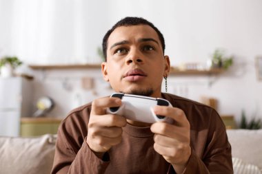 Yakışıklı genç adam oyuna odaklanmış, sıcak ve davetkar bir ev atmosferiyle çevrili..