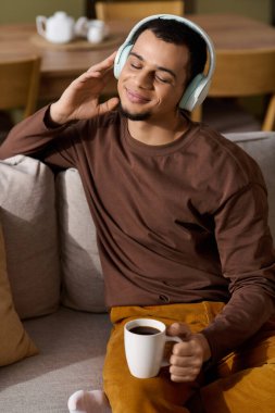 Rahat bir yuva ortamında, genç bir adam kahveyi yudumlarken müziğin tadını çıkarır ve kendini mutlu hisseder..