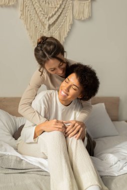 Sevgi dolu bir çift, sıcak dekore edilmiş bir odada yumuşak bir yatakta kucaklaşırken neşeyle gülümser..