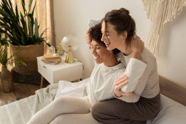 İki kadın sıcak bir kucaklaşmayı paylaşıyor, sevgi dolu sıcak bir yatak odasında birlikte gülüyorlar..