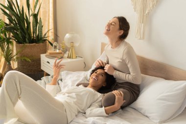 İki kadın, sakin bir yatak odasında neşeli bir anın tadını çıkarırken sevgilerini ve mutluluklarını ifade ederler..