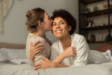 İki kadın, yatak odalarında sevgi ve mutluluk saçan şefkatli bir öpüşme ve kucaklaşmayı paylaşıyor..