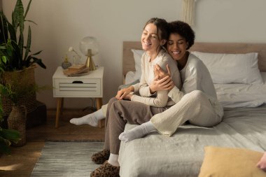 İki kadın, huzur ve sevgi ile çevrili, huzurlu yatak odalarında neşeyle kucaklaşıyor..