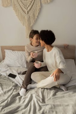 İki neşeli kadın barışçıl yatak odalarında kucaklaşırken aynı anda sıcak bardakları paylaşıyorlar..