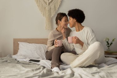 İki kadın, şık bir yatak odasında sıcak içkileri yudumlarken birbirlerine eşlik etmekten hoşlanırlar..