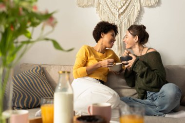 İki kadın gülüyor ve rahat mekanlarında yemek ve içeceklerin tadını çıkarırken rahat bir anı paylaşıyorlar..