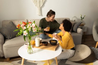 İki kadın, sıcak ve davetkar bir yaşam alanında içki ve kahvaltı eşliğinde birbirlerine eşlik etmekten hoşlanırlar..