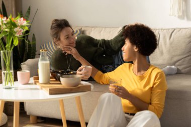 İki kadın birbirine eşlik etmekten hoşlanır. Sıcak bir oturma odasında gülüp içkilerini paylaşırlar..