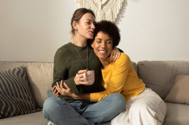 İki kadın evlerinde içkilerini yudumlarken rahat bir koltukta sevgi ve mutluluğu paylaşıyor..