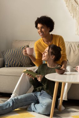İki neşeli kadın, sıcak içkilerini yudumlarken ve kitap okurken birbirlerine eşlik etmekten zevk alırlar..