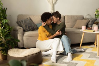 İki kadın sıcak, davetkar oturma odalarında sevgi ve rahatlıkla kucaklaşır..