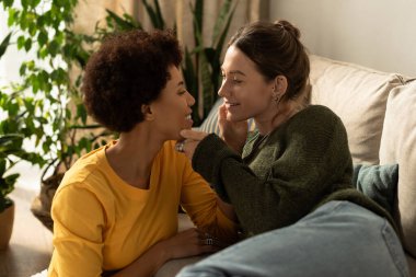 İki kadın, yumuşak bir kanepede otururken kahkaha ve aşkla dolu samimi bir anı paylaşıyor..