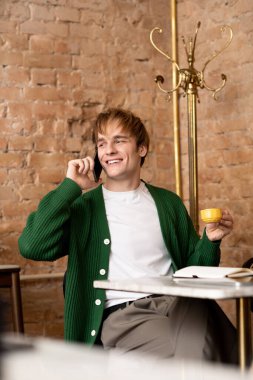 Sarışın genç adam kahve yudumlarken telefonuyla sohbet ediyor..