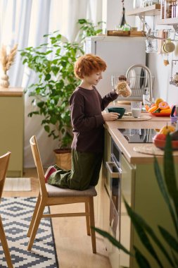 Çocuk sevinçle parlak mutfağını keşfeder, merak ve neşe dolu bir sandalyede dururken..