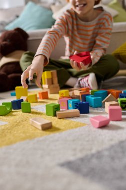 Neşeli küçük bir çocuk, neşeli yerinde yumuşak bir halıya parlak bloklar yığmaktan zevk alır..