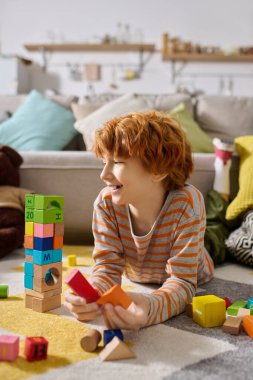 Neşeli bir çocuk rahat bir halıda oynarken renkli blokları dizmeye odaklanır..