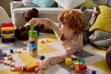 Neşeli bir çocuk parlak blokları yığmaya ve oyun alanında renkli bir kule yapmaya odaklanıyor..