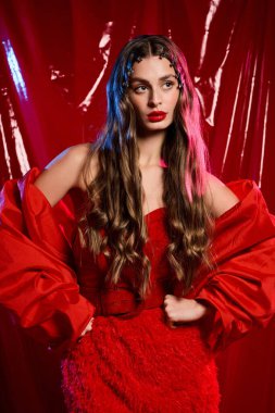 Şık bir genç kadın uzun saçlarıyla ve çarpıcı kırmızı elbisesiyle güzelliğini sergiliyor..