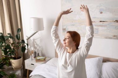 Neşeli genç bir kadın ışıkla dolu modern bir dairede kollarını açıyor..