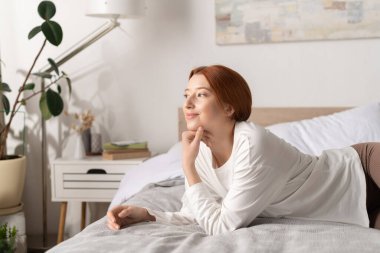 Genç bir kadın yatağında dinleniyor, şık dairesinde düşüncelere dalmış..