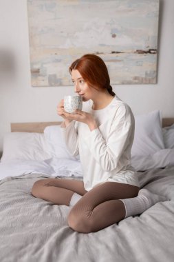 Kızıl saçlı genç bir kadın elinde kahveyle evde huzurlu bir anın tadını çıkarıyor..