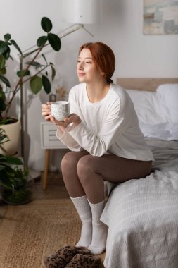 Kızıl saçlı genç bir kadın evde sakin bir sabah geçirir, özenle çayını yudumlar..