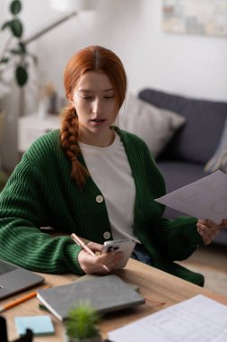 Canlı kızıl saçlı genç bir kadın şık dairesinde oturuyor, birden fazla işi var..