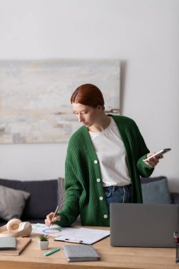 Kızıl saçlı genç kadın rahat dairesinin tadını çıkarırken çizim yapmaya odaklanmış..