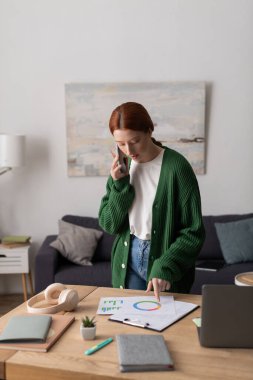 Genç, kızıl saçlı bir kadın, sıcak dairesinde çalışıyor. Fikirlerini birleştiriyor..