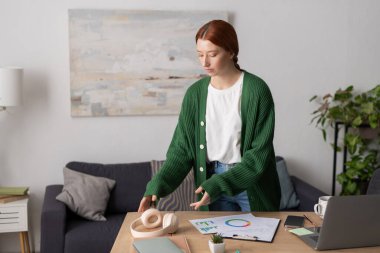 Kızıl saçlı bir kadın modern dairesinde oturup kulaklıkla dinliyor..