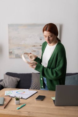 Gündelik giysiler içinde kızıl saçlı genç bir kadın şık bir yaşam alanında kulaklıklarını keşfediyor..