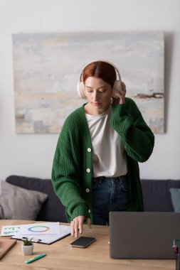 Canlı kızıl saçlı genç bir kadın modern dairesinde dinlenirken müzik dinliyor..