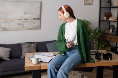 Kızıl saçlı sıradan giyinmiş, şık evinde rahat bir an geçirip müzik dinliyor..