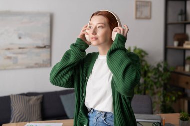 Kızıl saçlı genç bir kadın şık dairesinde dikkatle müzik dinliyor..