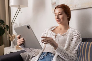 Rahat, kızıl saçlı genç bir kadın rahat bir apartman dairesinde tabletle meşgul oluyor..