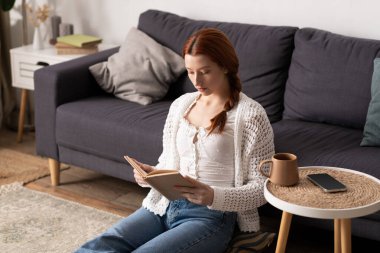 Rahat, modern bir dairede, kızıl saçlı genç bir kadın kitap okurken rahatlıyor..