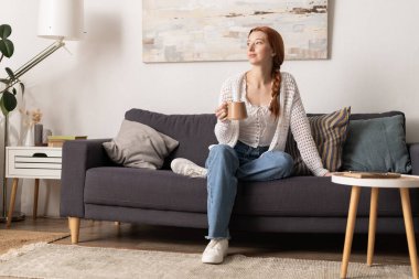 Rahat ve rahat, kızıl saçlı genç bir kadın çayını yudumluyor, evinde rahat ediyor..