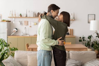 Bir erkek ve kadın, modern evlerinde sevgiyle kucaklaşıp mutluluk ve bağ yayıyorlar..