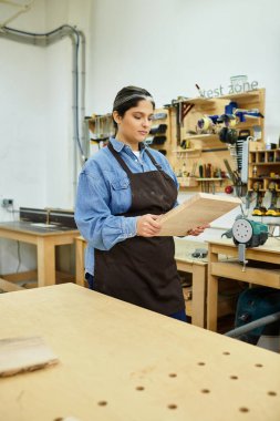 Güzel bir genç kadın atölyede duruyor, sanata odun eklemeye odaklanmış..