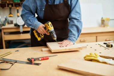 Genç bir kadın, çeşitli atölye araçlarıyla çevrili, parlak bir gülümsemeyle tutkuyla odunları deliyor..