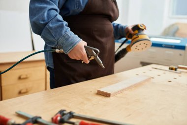 Güzel genç bir kadın, davetli atölyesinde ahşap bir parça üzerinde çalışırken zımpara makinesi kullanıyor..