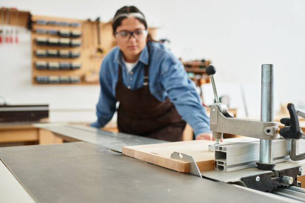 A beautiful young woman focuses intently while working on a woodworking project at a workshop.