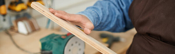 A young woman shapes wood in her workshop, surrounded by tools.