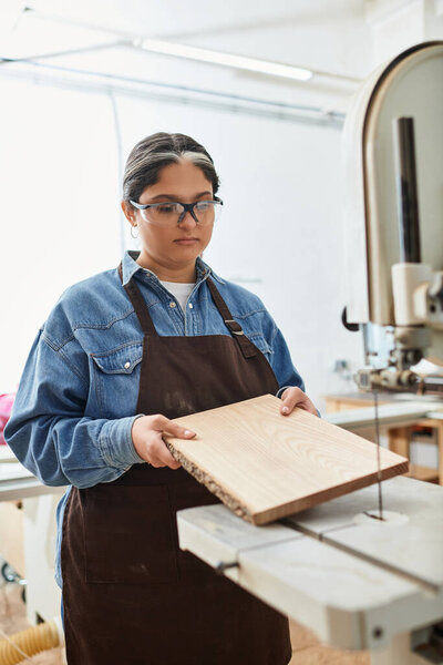 A young woman focuses intently on working with a piece of wood in a vibrant workshop setting.
