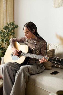 Örgülü genç siyah bir kadın şık dairesinde gelişigüzel gitar çalıyor..