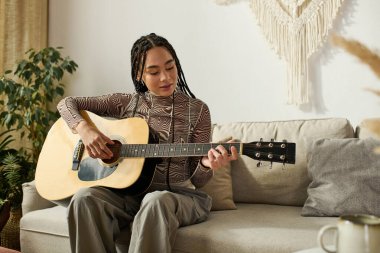 Gitarını tıngırdatan genç bir kadın, rahat bir dairede yeteneğini ve tarzını sergiliyor..