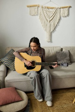 Genç bir Afrikalı Amerikalı kadın şık dairesinde gitar çalıyor, etrafı hoş dekorlarla çevrili..