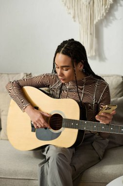 Örgülü genç Afrikalı Amerikalı kadın evde dinlenirken gitar çalmayı seviyor..